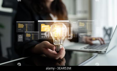 A business professional holds a glowing light bulb while interacting with digital folders, symbolizing creativity and modern technological solutions Stock Photo
