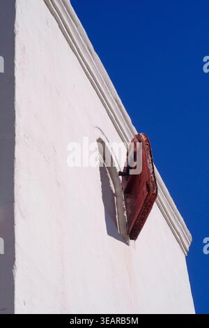 White painted building against a blue sky without clouds and a small window opening with a red door. Stock Photo
