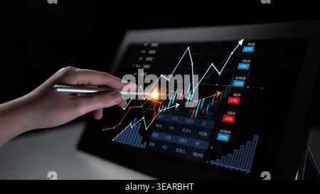 A close-up of a hand using a stylus on a digital screen, displaying stock market graphs and data visualization for professional financial analysis and Stock Photo