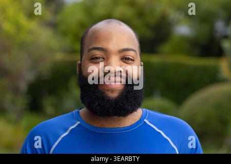 African American man standing and smiling while wearing blue athletic shirt in backyard garden. Headshot, portrait, bearded, activewear, outdoor, boke Stock Photo