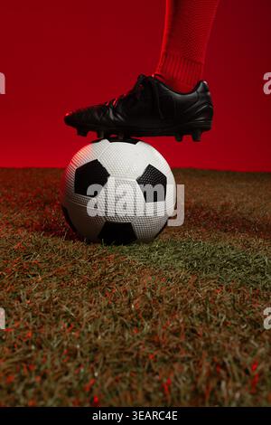 African American female balancing right foot in black-cleat and red-sock on soccer-ball studio turf. Athlete, ball, closeup, leather, crimson, rimligh Stock Photo