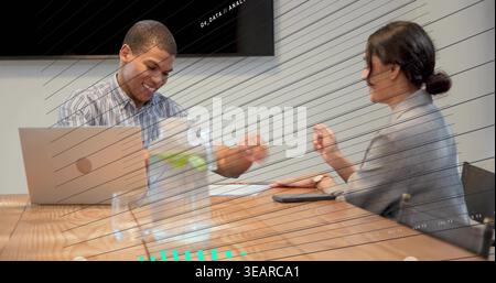 Leaning colleagues in striped shirt and gray blazer bumping fists at conference table with laptop. Meeting, teamwork, collaboration, minimalist, board Stock Photo