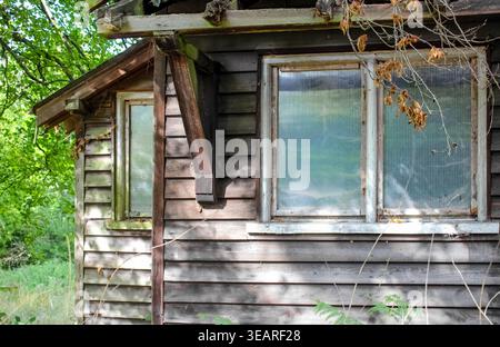 Eversley, United Kingdom - Sep 21, 2025: An old, abandoned wooden cabin in Eversley with weather-worn siding and translucent ribbed plastic sheets. Stock Photo