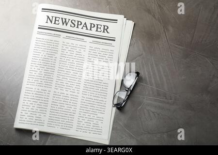 Newspaper and glasses on grey table, flat lay Stock Photo