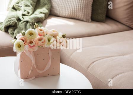 Delicate lifestyle composition featuring a quilted pink gift bag filled with cream and blush ranunculus flowers, accented by ribbon handles and decora Stock Photo