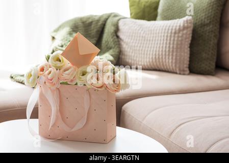 Delicate lifestyle composition featuring a quilted pink gift bag filled with cream and blush ranunculus flowers, accented by ribbon handles and decora Stock Photo