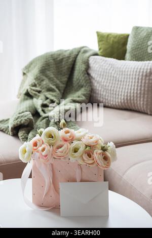 Delicate lifestyle composition featuring a quilted pink gift bag filled with cream and blush ranunculus flowers, accented by ribbon handles and decora Stock Photo