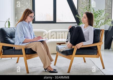 Professional female psychologist taking notes during a consultation with a young female client Stock Photo
