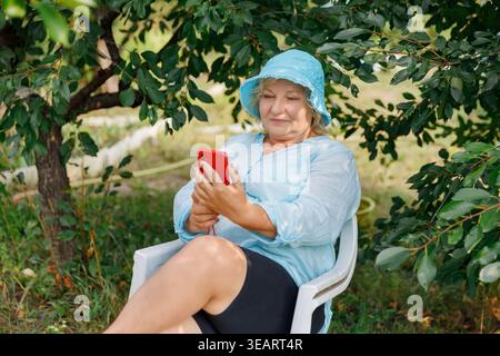 Mature woman having video call on phone in summer garden Stock Photo