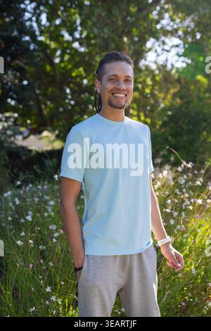 African American man standing in park wearing light blue tee gray sweats showing watch, bracelet. Outdoor, meadow, greenery, canopy, grasses, lifestyl Stock Photo