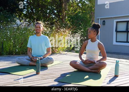 African American friends practicing seated yoga on deck with green mats, tall bottles in sportswear. Outdoor, wellness, mindfulness, serenity, nature, Stock Photo