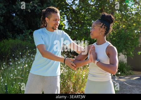 African American fitness partners practicing move on sunlit path, showing smartwatch and bracelet. Duo, workout, trainer, outdoor, garden, foliage, po Stock Photo