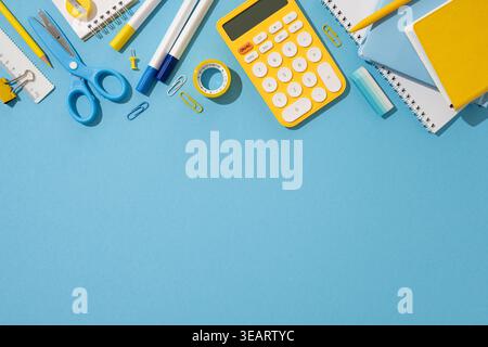 Flat lay of school supplies including calculator, scissors, and notebooks on a blue background Stock Photo