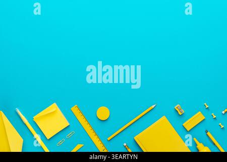 Top view photo of yellow stationery over turquoise blue background with copy space. Flat lay image of different stationary objects as back to school c Stock Photo