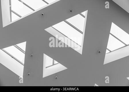 Minimal modern ceiling design with triangular skylights creating a geometric pattern of natural light and shadow. Black and white architectural compos Stock Photo
