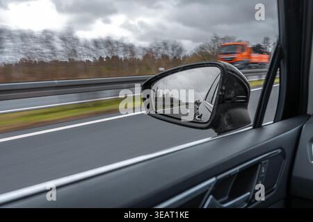 View of the road through a car side mirror. The vehicle moves on a highway in cloudy weather. Stock Photo