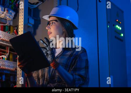 Female electrical engineer inspecting power system on tablet near switchboard. Digital control. Stock Photo