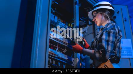 Female electrician inspecting electrical switchboard using tablet. Engineering service. Stock Photo