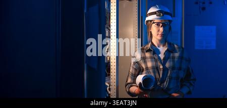 Electrical standing near industrial switchboard holding system blueprint. Engineering portrait. Stock Photo