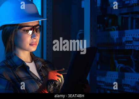 Electrical engineer analyzing power system using tablet near switchboard. Technical inspection. Stock Photo