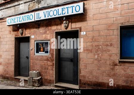 Exterior of Cineteatro Il Vicoletto in Cagliari, Sardinia. Stone facade with gray doors, theater masks, and a blue-lettered sign on a narrow street. Stock Photo