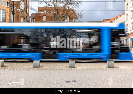 Blue tram moving fast past city buildings. Public transport in motion on an urban street. Stock Photo