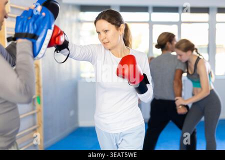 Woman in boxing gloves practices punches with trainer in mitts in sport club during family training Stock Photo