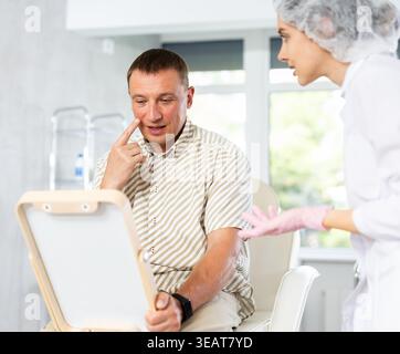 Man looks in mirror and rejoices at successful treatment of dermatological problems of face Stock Photo