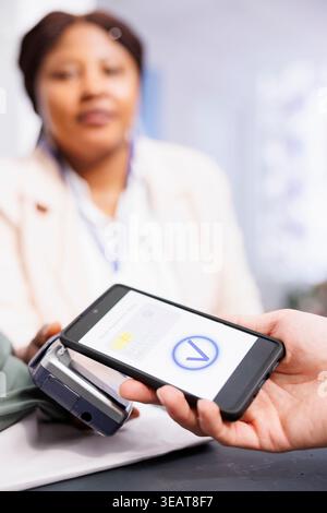 Contactless smartphone payment. African American woman cashier holding pos terminal checking out customer in retail store. Close up of male hand holding cellphone paying with mobile device Stock Photo