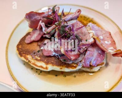 Close-up of crispy fried bacon served on top of a pancake, presented on a white plate. Stock Photo