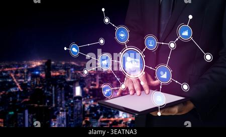 A businessman stands in front of a captivating city skyline at night, engaging with a digital tablet displaying network connections and data Stock Photo