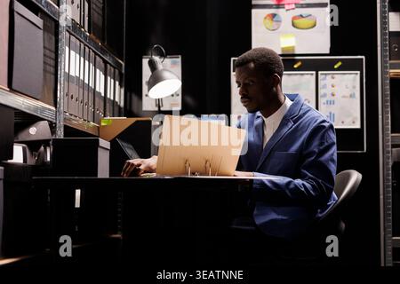 Corporate employee working at accountancy record, reading management documents in arhive room. African american businessman checking administrative report, analyzing bureaucracy files Stock Photo
