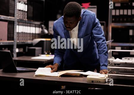 African american manager working at accountancy report, analyzing administrative files in company repository. Businessman checking bureaucracy record, searching for management research Stock Photo