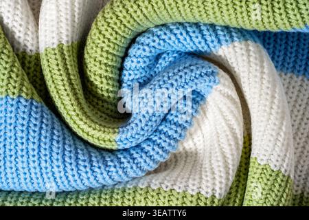 Close-up sweater texture in blue, white and pastel green color, striped knitted fabric in spiral swirl folds. Concept of textile detail synthetic knit Stock Photo
