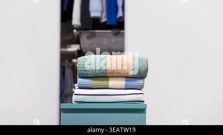 Folded colorful striped knitted woolen sweaters with open wardrobe on light gray background. Concept of wardrobe organization, seasonal clothing stora Stock Photo