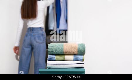 Folded knitted sweaters with woman near open wardrobe on light gray background. Concept of wardrobe organization, seasonal changeover, clothing sortin Stock Photo