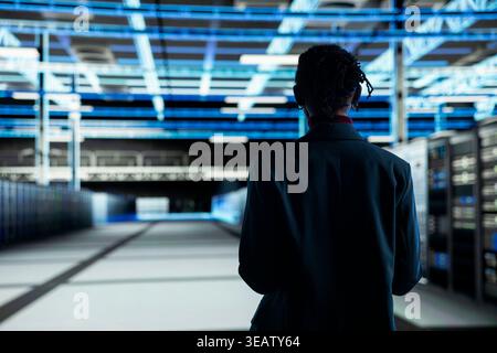 Admin walking in data center, configuring server settings with software. IT professional in modern high tech server hub doing maintenance tasks on infrastructure electronics Stock Photo