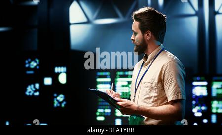 Admin walking in data center supporting AI through high performance computing, hosting specialized storage and networking hardware. Engineer ensuring server room internal hardware functions properly Stock Photo