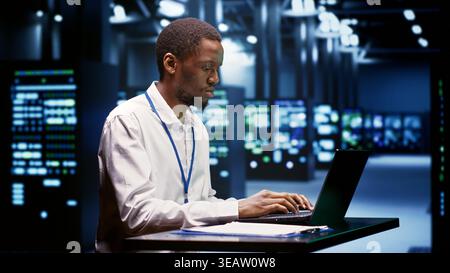Computer scientist using laptop to debug servers cabinets helping companies manage databases, host websites and store files. Repairman reviewing high tech facility used for high performance computing Stock Photo