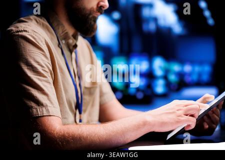 Certified electrician using tablet to examine blade servers for power fluctuations. Licensed professional monitoring data center devices, identifying potential vulnerabilities, close up Stock Photo