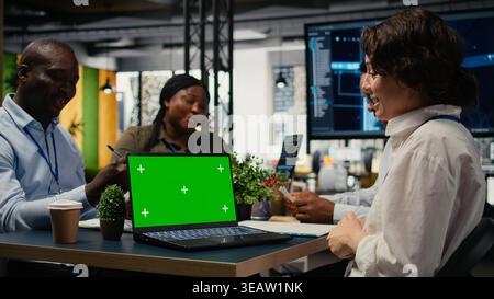Green screen laptop used by programmers in startup office leveraging AI tech to gain competitive edge. Management doing meeting to discuss training deep learning models using mockup notebook, camera A Stock Photo