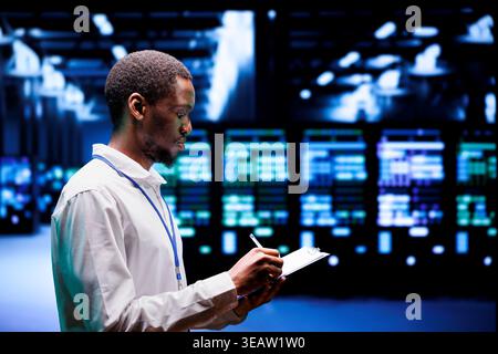 Adept supervisor overseeing server hub using renewable sources to minimize consumption and reduce overall facility carbon footprint. African american technician working in eco friendly data center Stock Photo