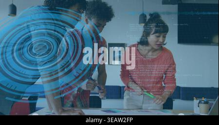 Reviewing layouts, three colleagues leaning over table in office with coral sweater, HUD overlay Stock Photo