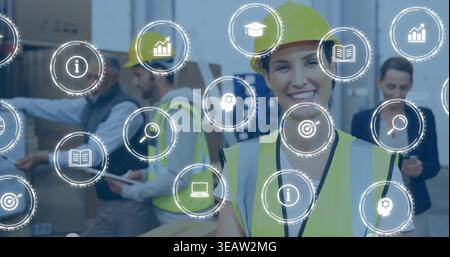 Smiling warehouse worker in hard hat and hi-vis vest checking boxes using tablet, overlay icons Stock Photo