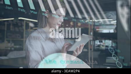 Holding tablet, adult Asian woman tapping bar chart on glass in open office, wearing light blouse Stock Photo