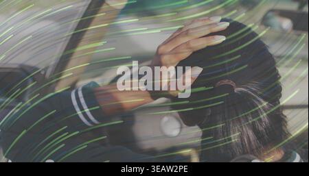 Sitting Indian woman wearing dark jacket, striped cuff, touching hair in car, green streaked glass Stock Photo