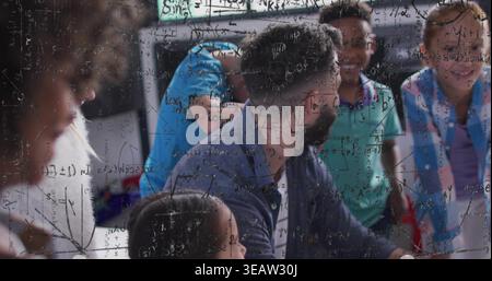 Talking bearded facilitator in classroom wearing navy shirt guiding children at table, math overlay Stock Photo