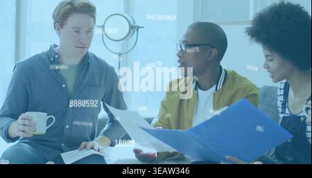 Reviewing prints, three coworkers in casual jacket, overalls on couch in lounge with blue folder Stock Photo