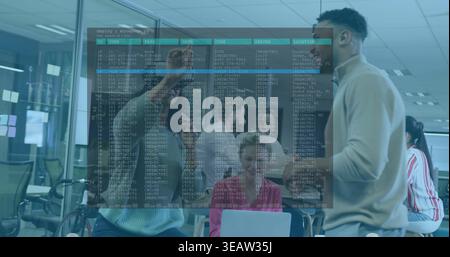 Pointing coworker wearing sweater explaining code overlay on glass partition in open office, laptop Stock Photo