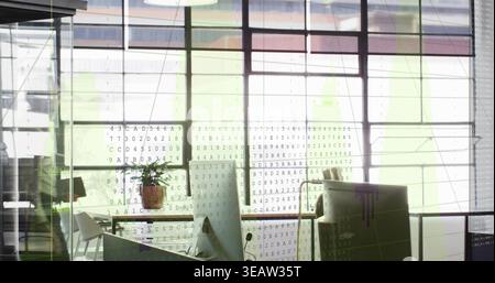 Displaying desk cluster with monitor and potted plant in open-plan office, showing code overlay Stock Photo